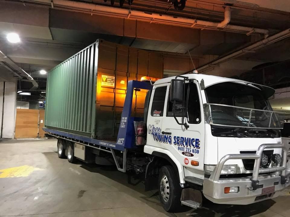 A Tow Truck With a Green Container on the Back is Parked in a Parking Garage — Mick's Towing Service Pty Ltd in Carrara, QLD