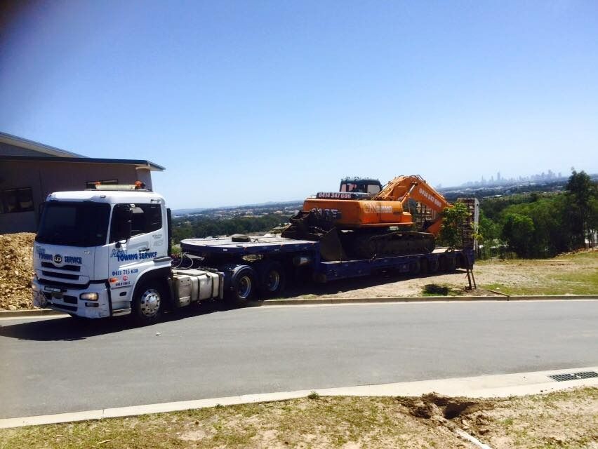 A White Truck is Carrying a Large Orange Excavator on a Flatbed Trailer — Mick's Towing Service Pty Ltd in Carrara, QLD