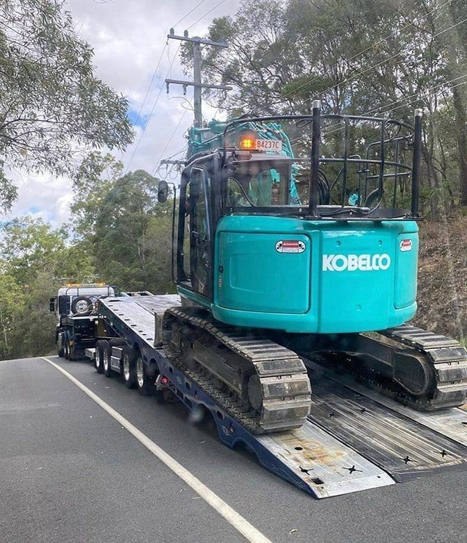A Blue Excavator is Being Transported on a Flatbed Truck — Mick's Towing Service Pty Ltd in Carrara, QLD