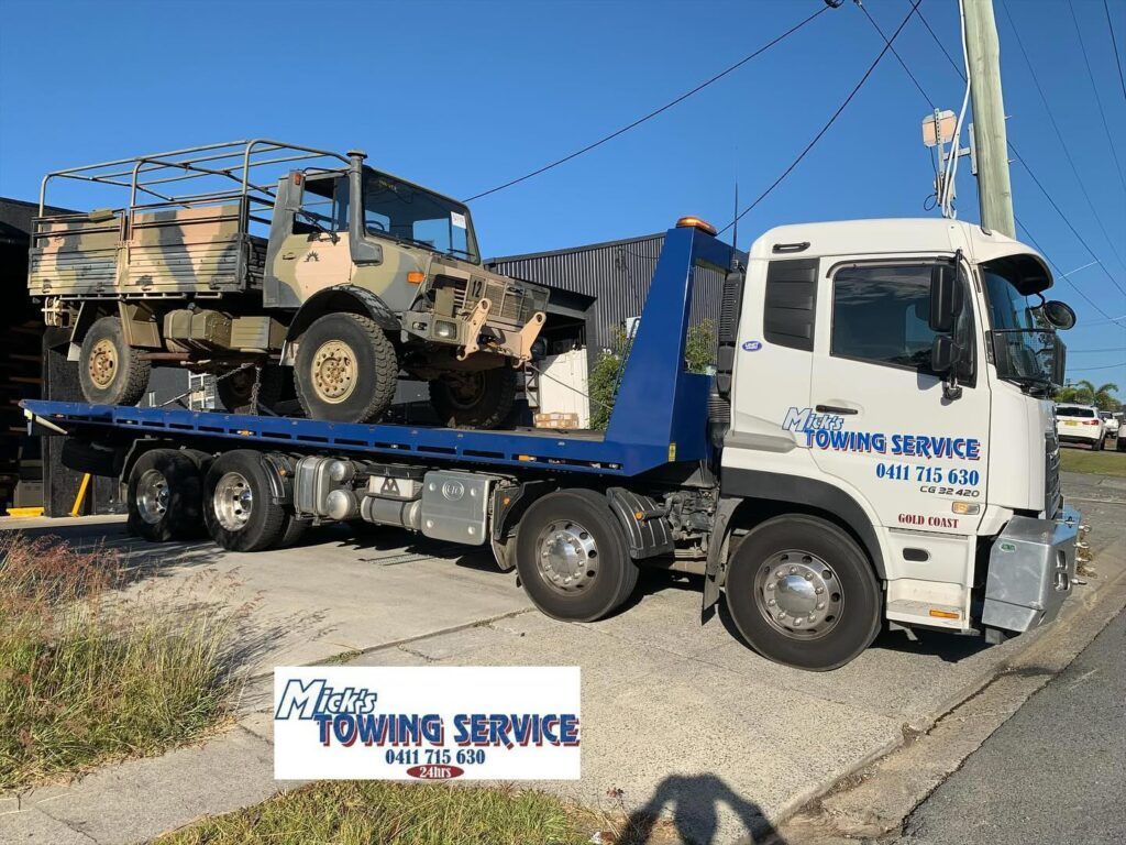 A Towing Truck is Carrying Two Military Vehicles — Mick’s Towing Service Pty Ltd in Carrara, QLD