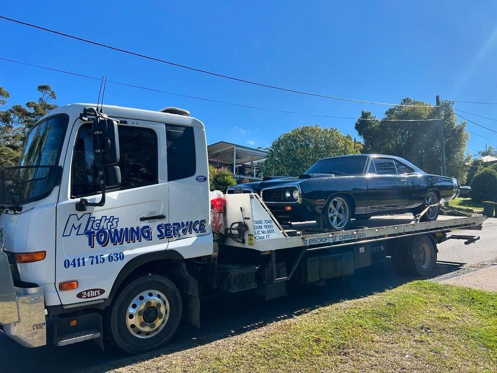 A Towing Truck is Carrying a Black Car on the Back of It — Mick’s Towing Service Pty Ltd in Carrara, QLD