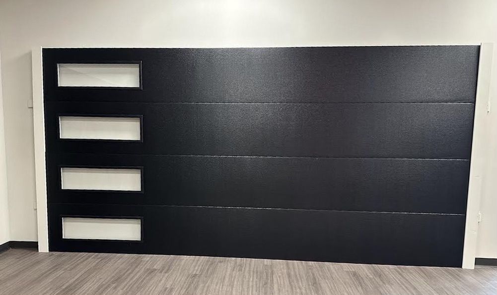 A black garage door is sitting on a wooden floor in a room.