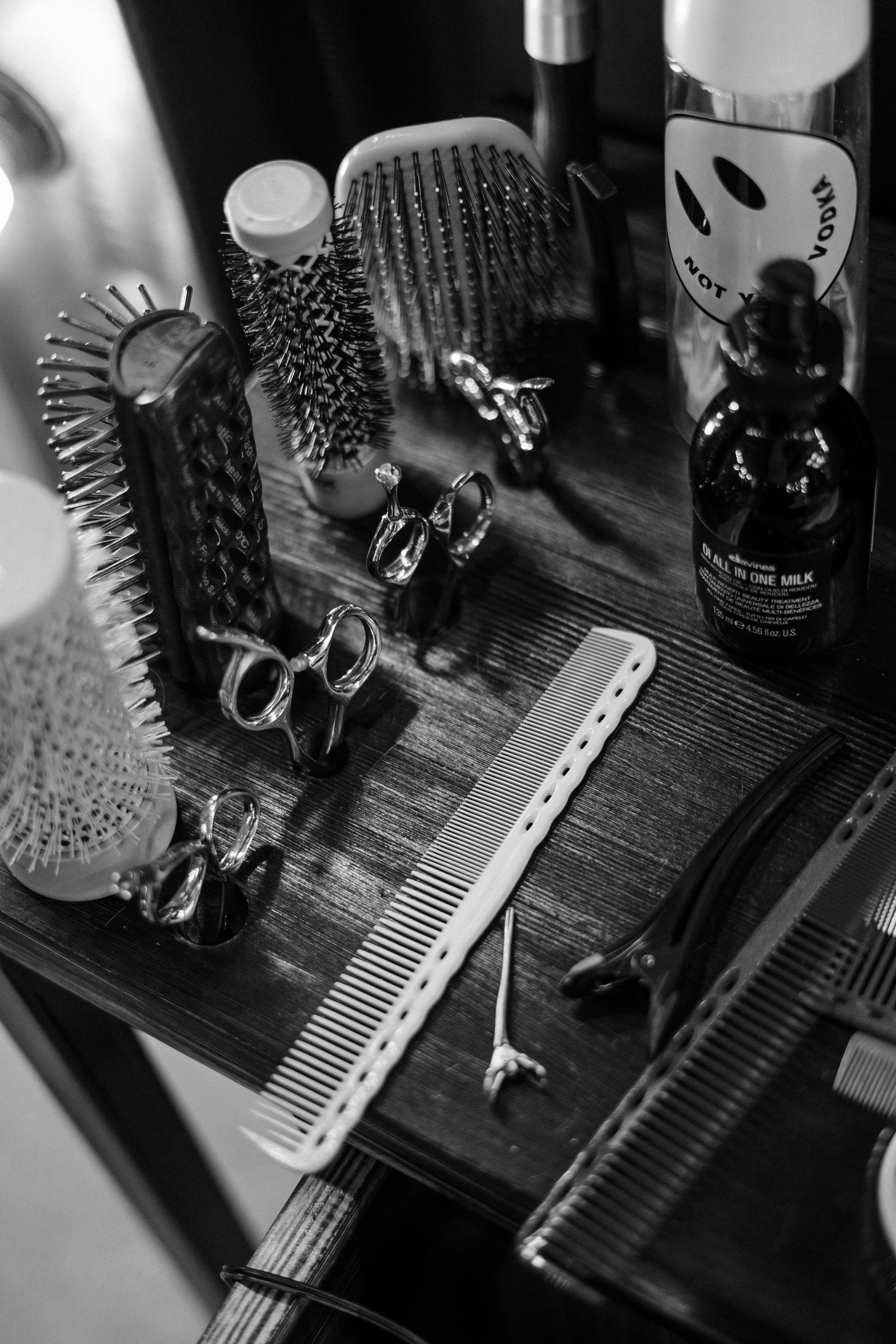 Black and white photo: Various hair styling tools on a dark wooden surface. Combs, clips, and brushes are visible.