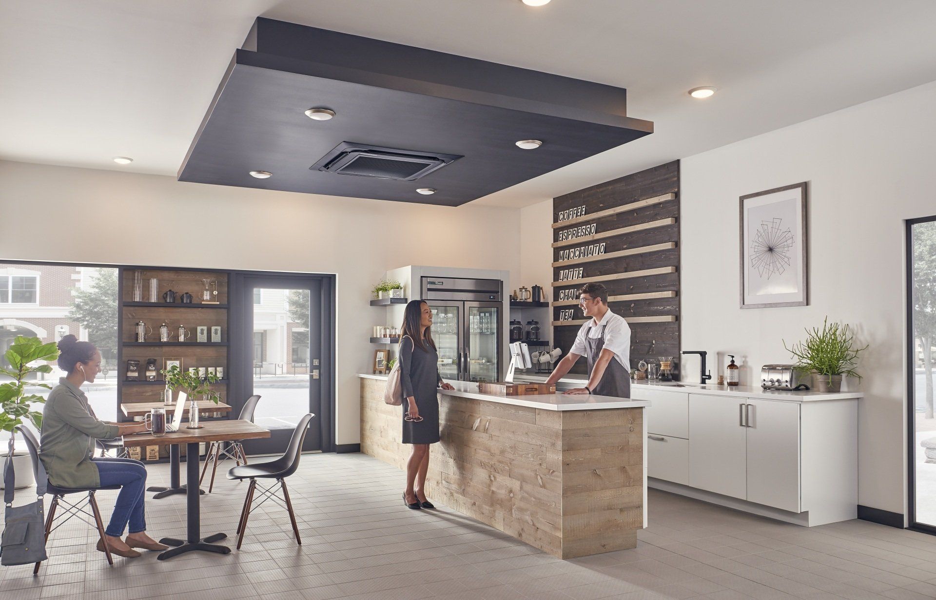 Coffee shop interior: Customers at counter and table. Bright space, light wood and white surfaces.