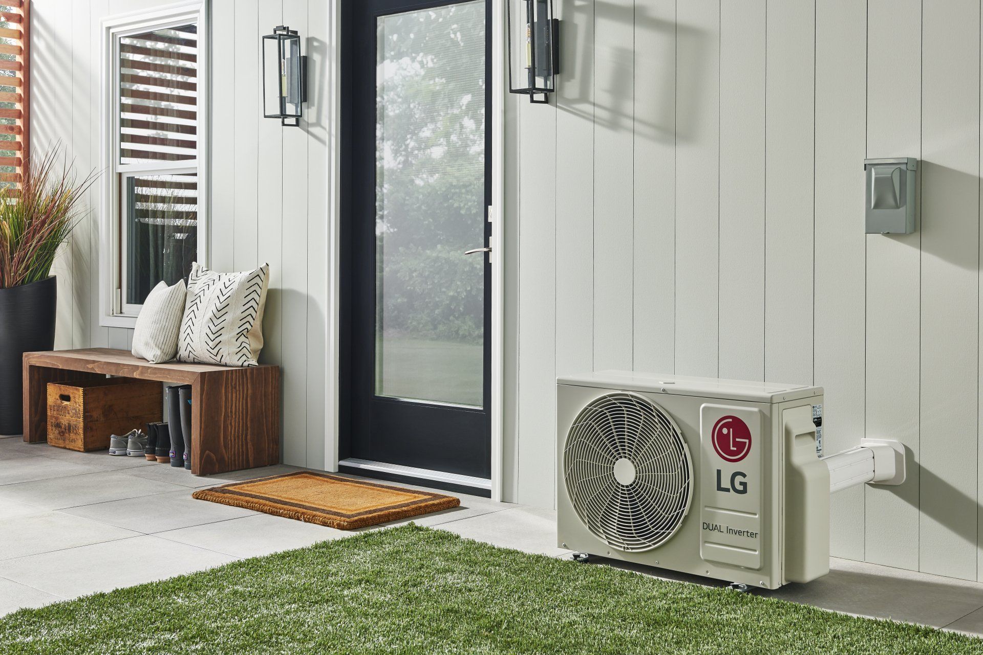 LG outdoor air conditioner unit near a doorway, on a patio with greenery.