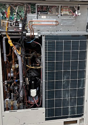 Open Daikin VRV air conditioning unit interior, revealing copper pipes, electrical wiring, and a black compressor.