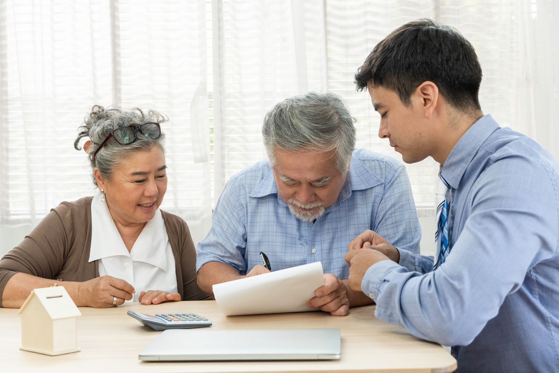 A senior man signing a document with support from his wife sitting at a table with an advisor.