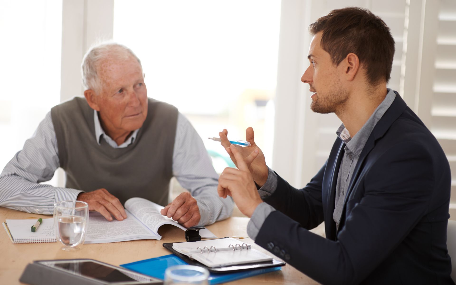 An advisor talking to a senior man with documents and a tablet on a table.