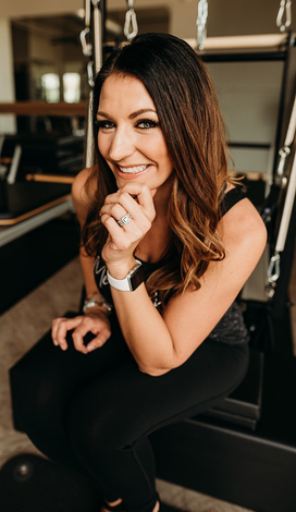 A woman is sitting on a pilates machine and smiling.