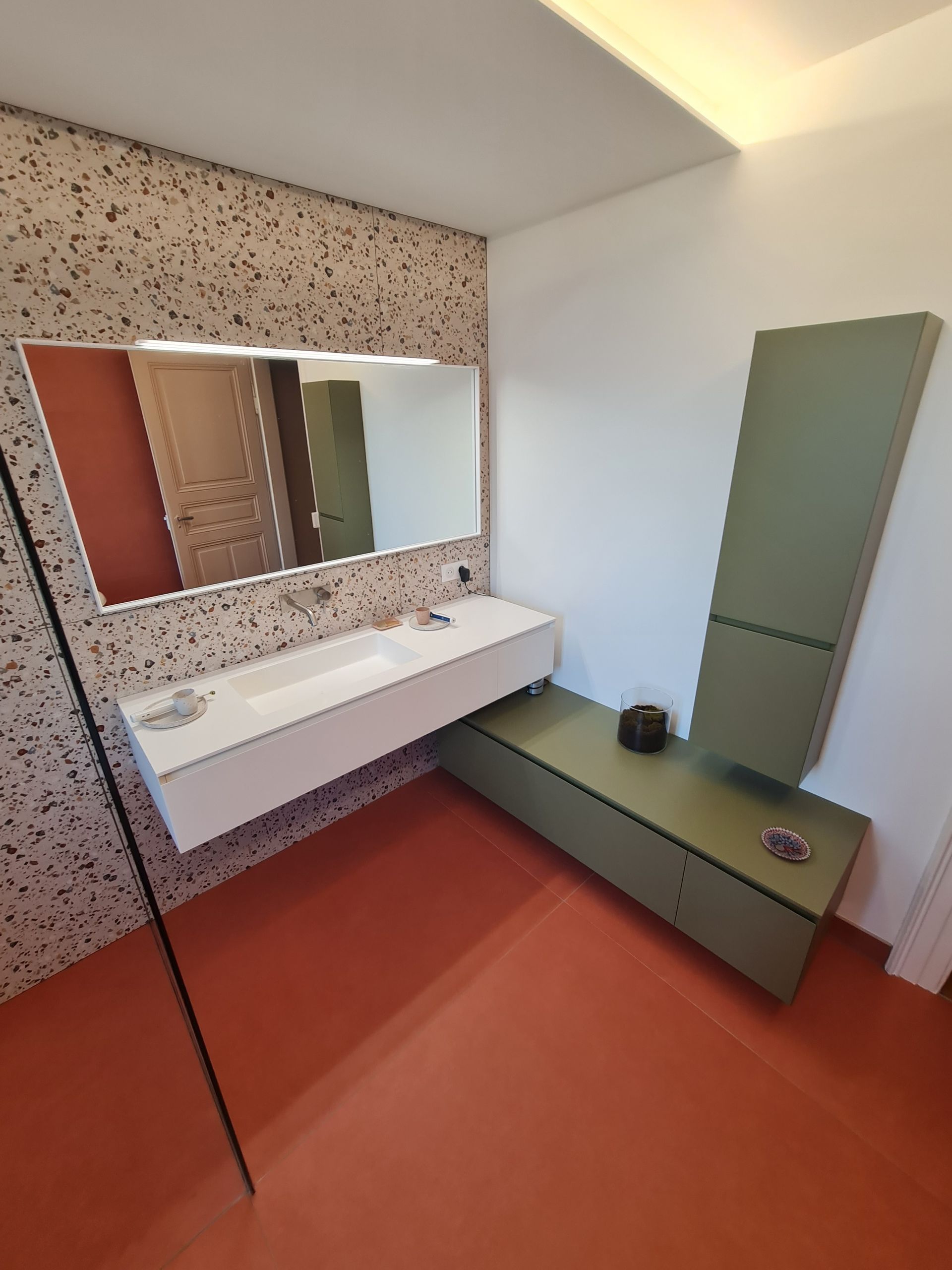 Une salle de bain avec un lavabo, un miroir et des armoires vertes.