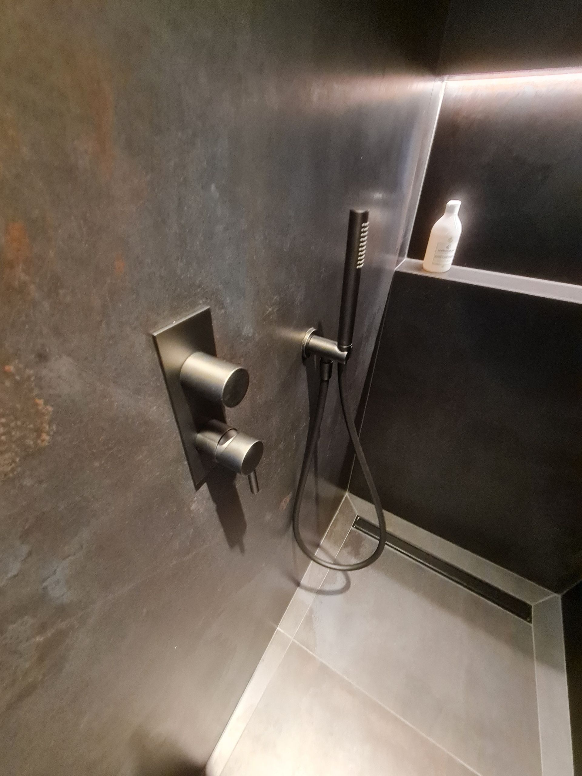 Une salle de bain avec un pommeau de douche et un distributeur de savon sur l'étagère.