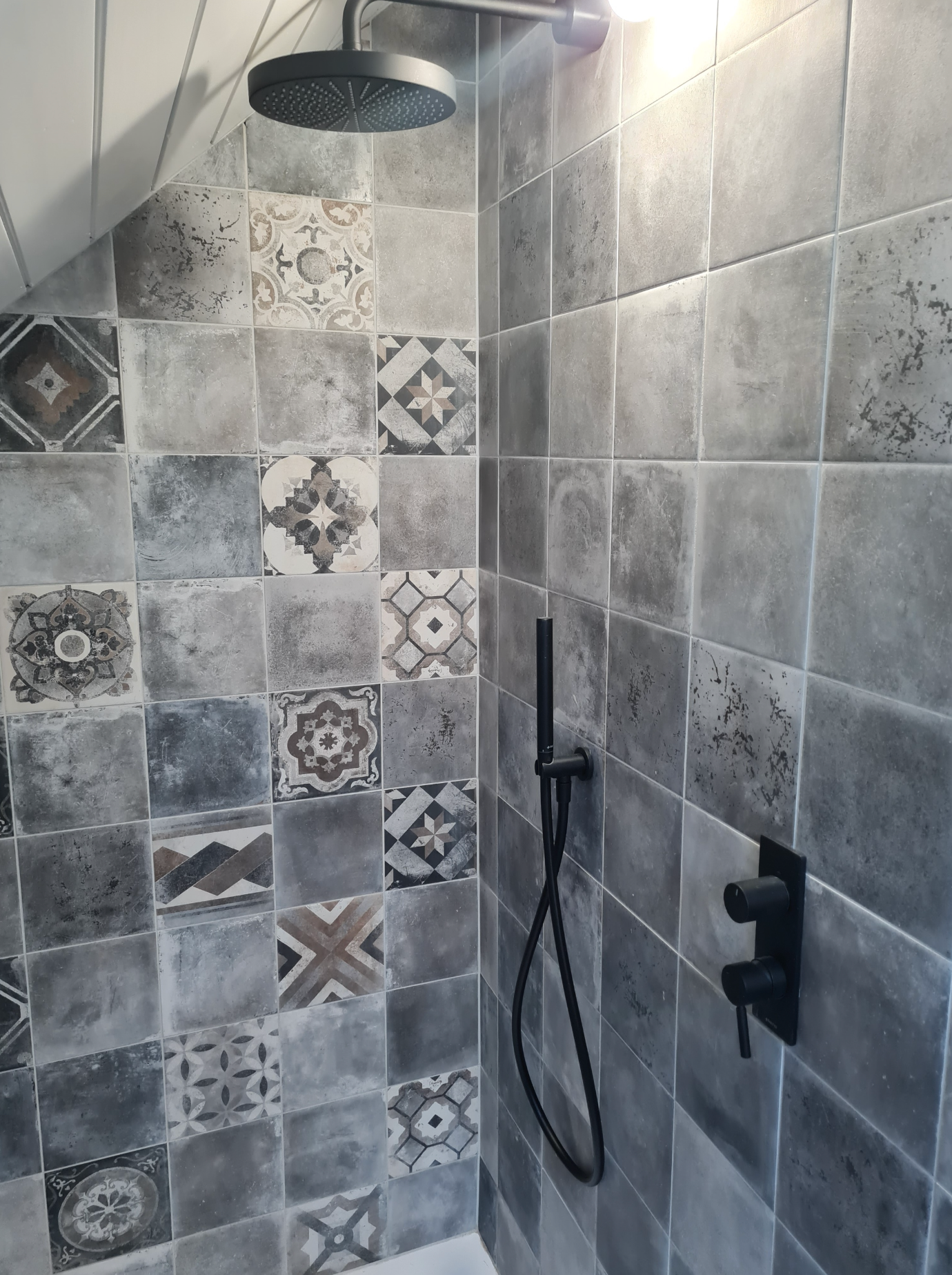 Une douche avec carrelage gris et pommeau de douche noir.