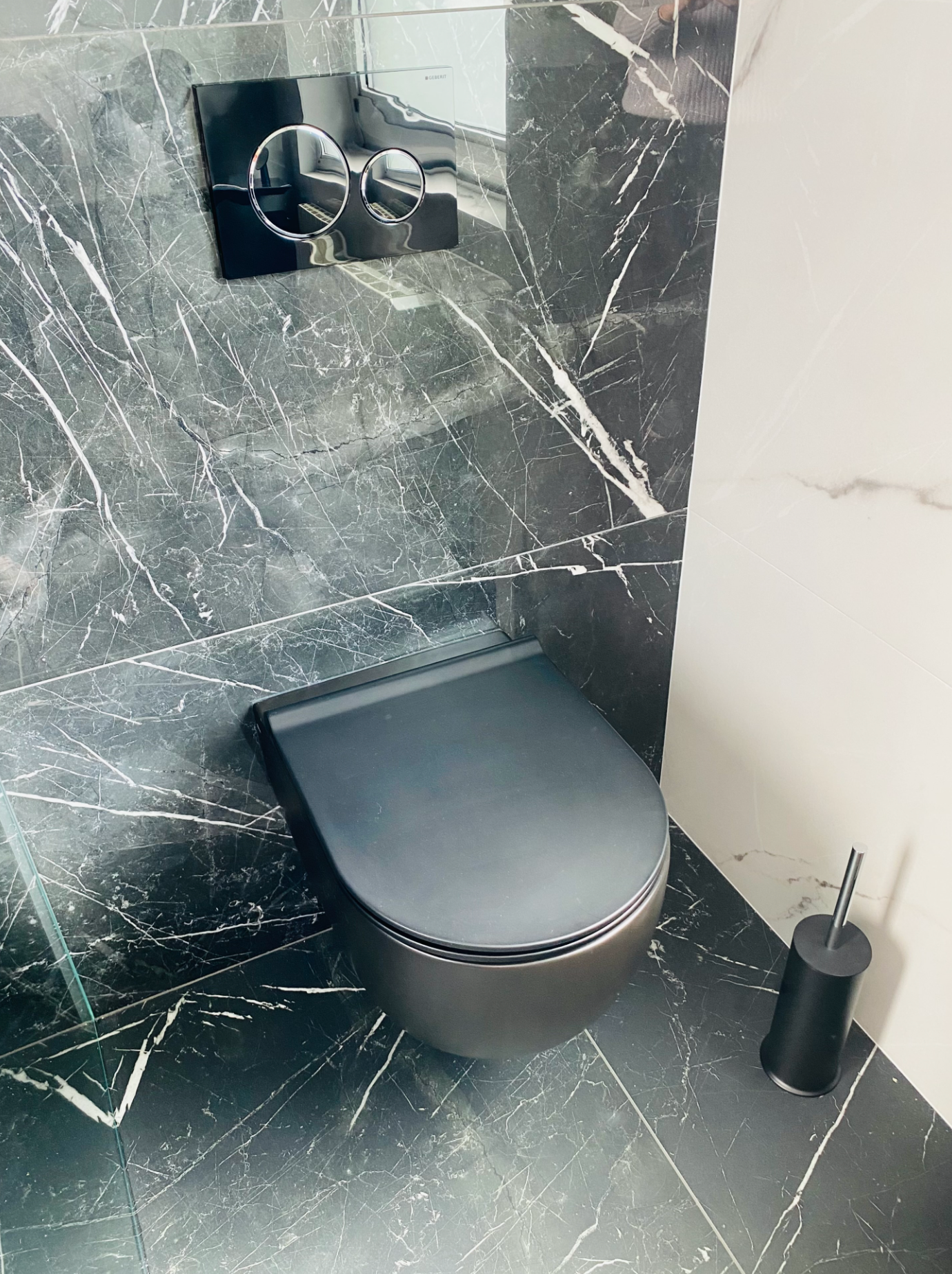Une toilette noire est installée dans une salle de bain à côté d'un mur en marbre.