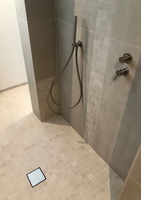 Une salle de bain avec une douche et un drain carré au sol.