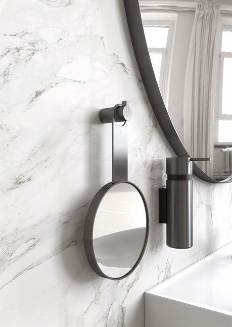 Miroir ovale et distributeur de savon fixés sur un mur en marbre. Le miroir est maintenu par un bras métallique. Une fenêtre est visible en arrière-plan.