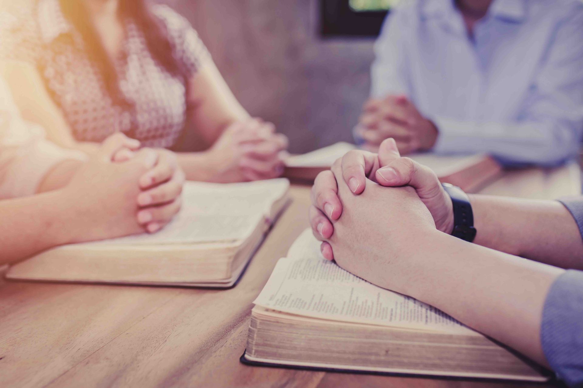 A group of people are sitting at a table with their hands folded in prayer.