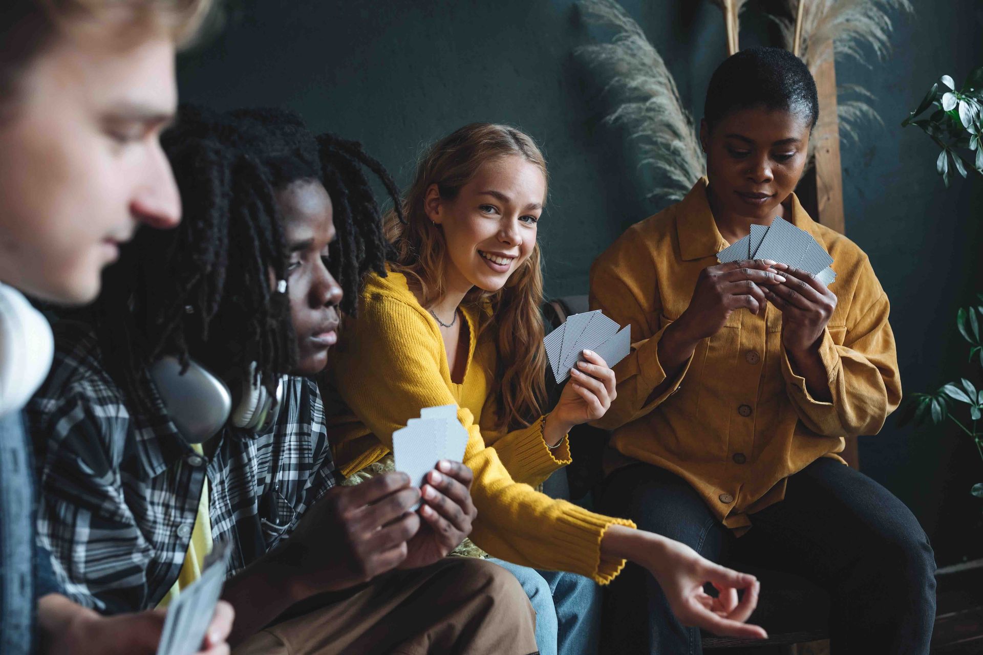 A group of young people are sitting on a couch playing cards.
