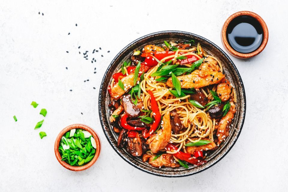 Stir fry egg noodles with chicken, sweet paprika, mushrooms, chives and sesame seeds in bowl. Asian cuisine dish.