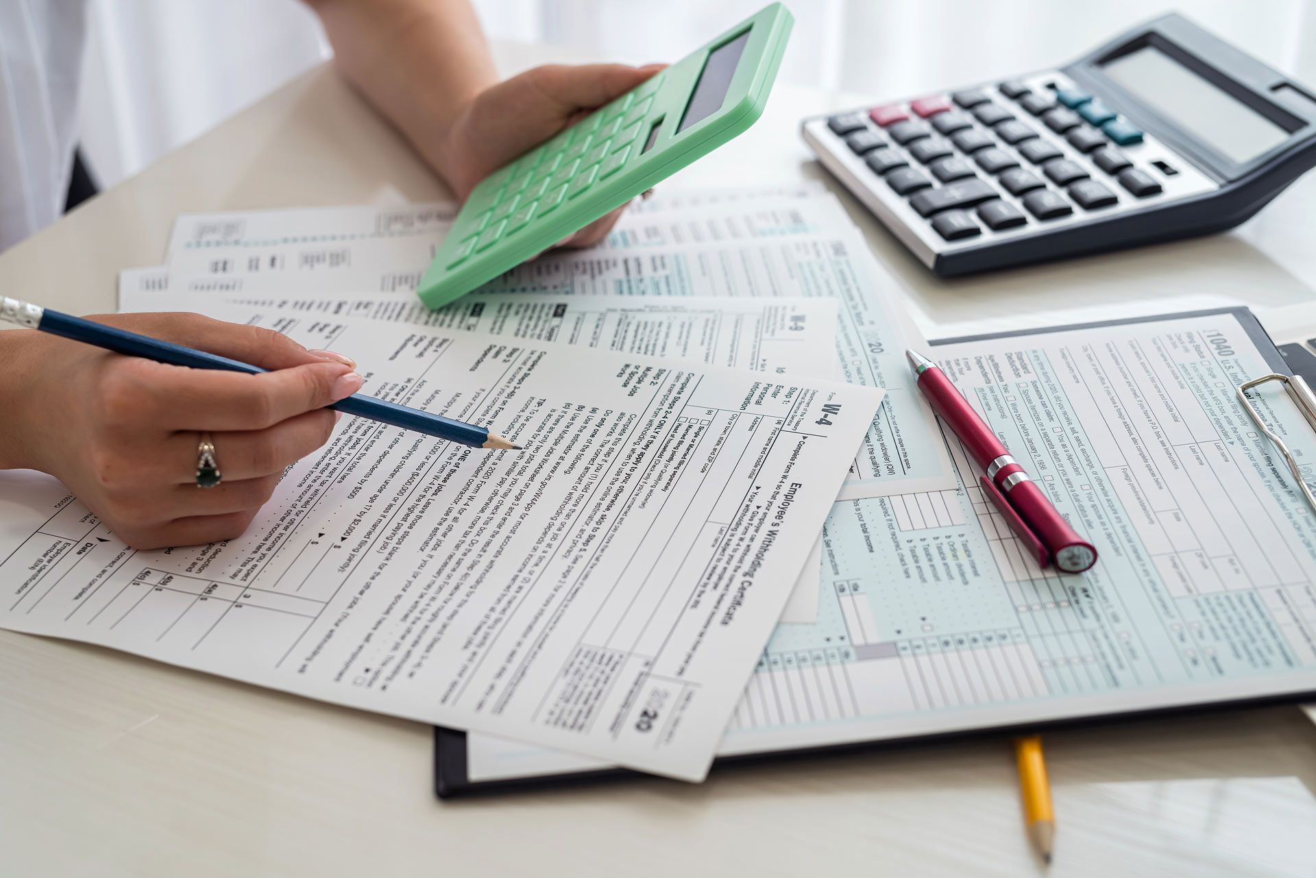 Person calculating taxes with a calculator and pen, surrounded by tax forms.