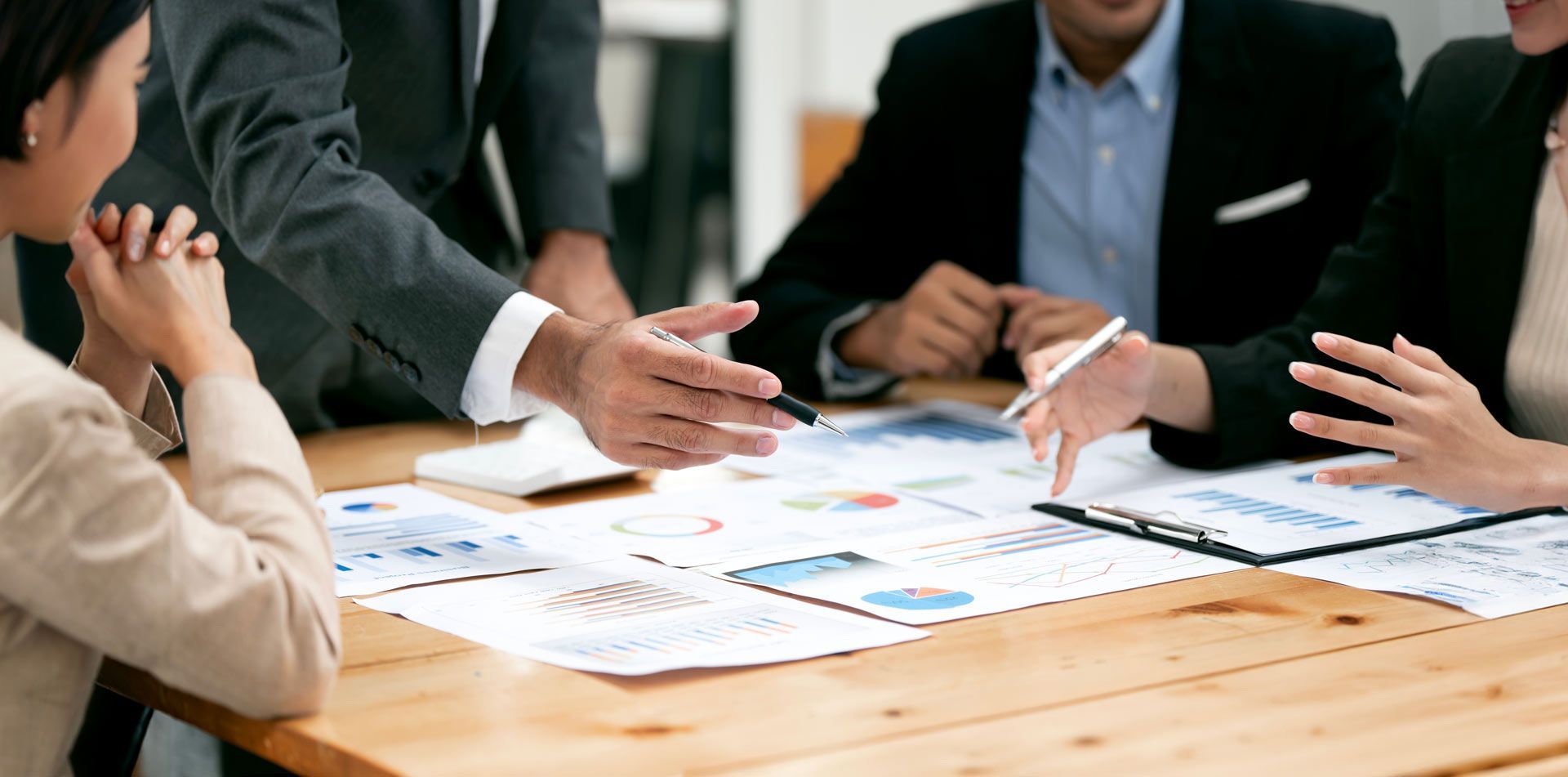 Businesspeople review financial documents at a wooden table in an office.