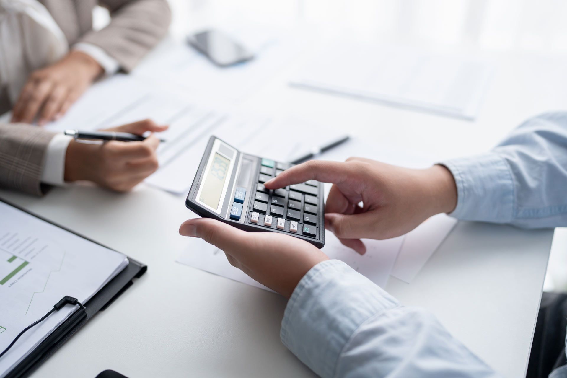 Hands using calculator on a table with documents. Another person writes with pen.