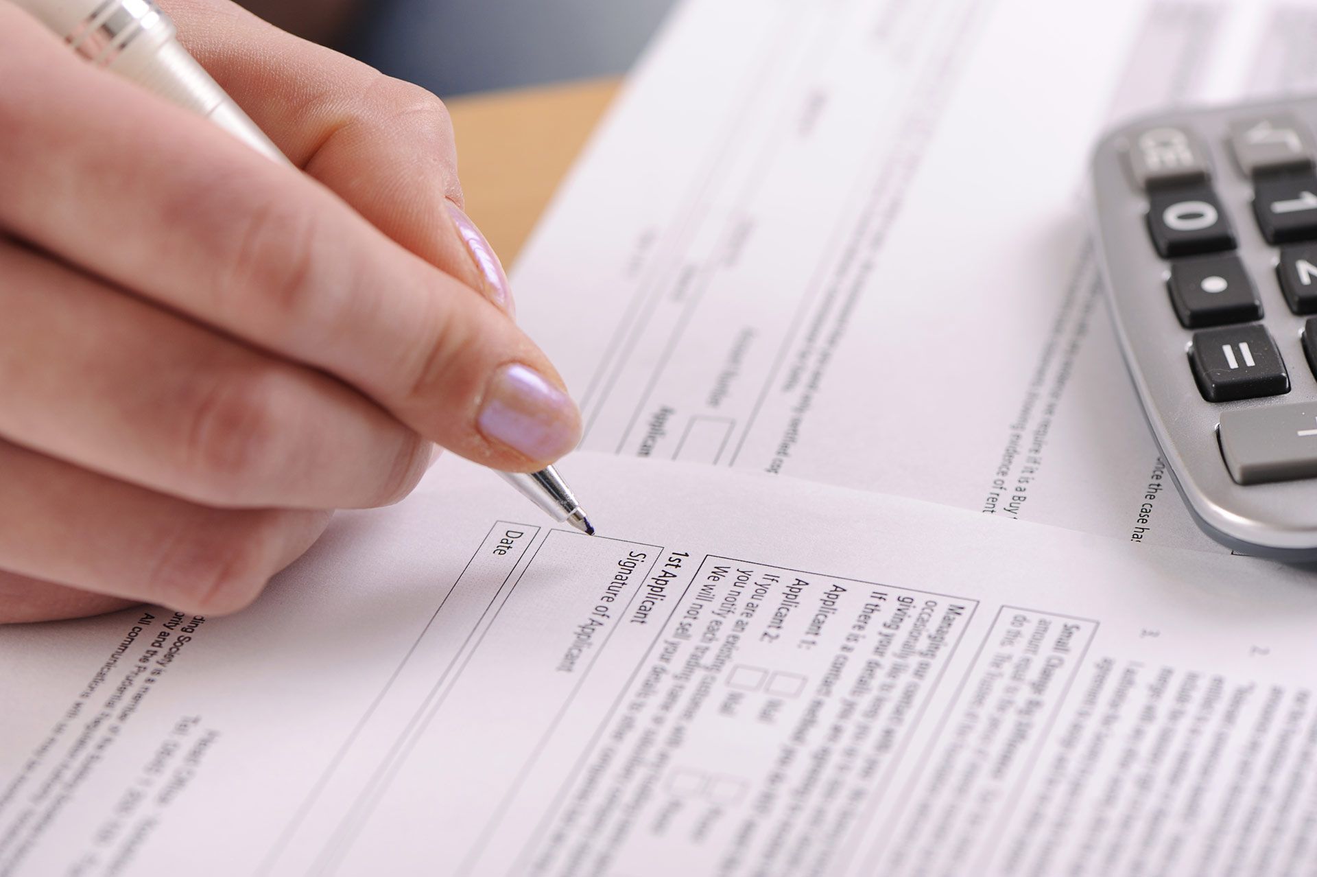 Hand writing on paper with a pen next to a calculator.