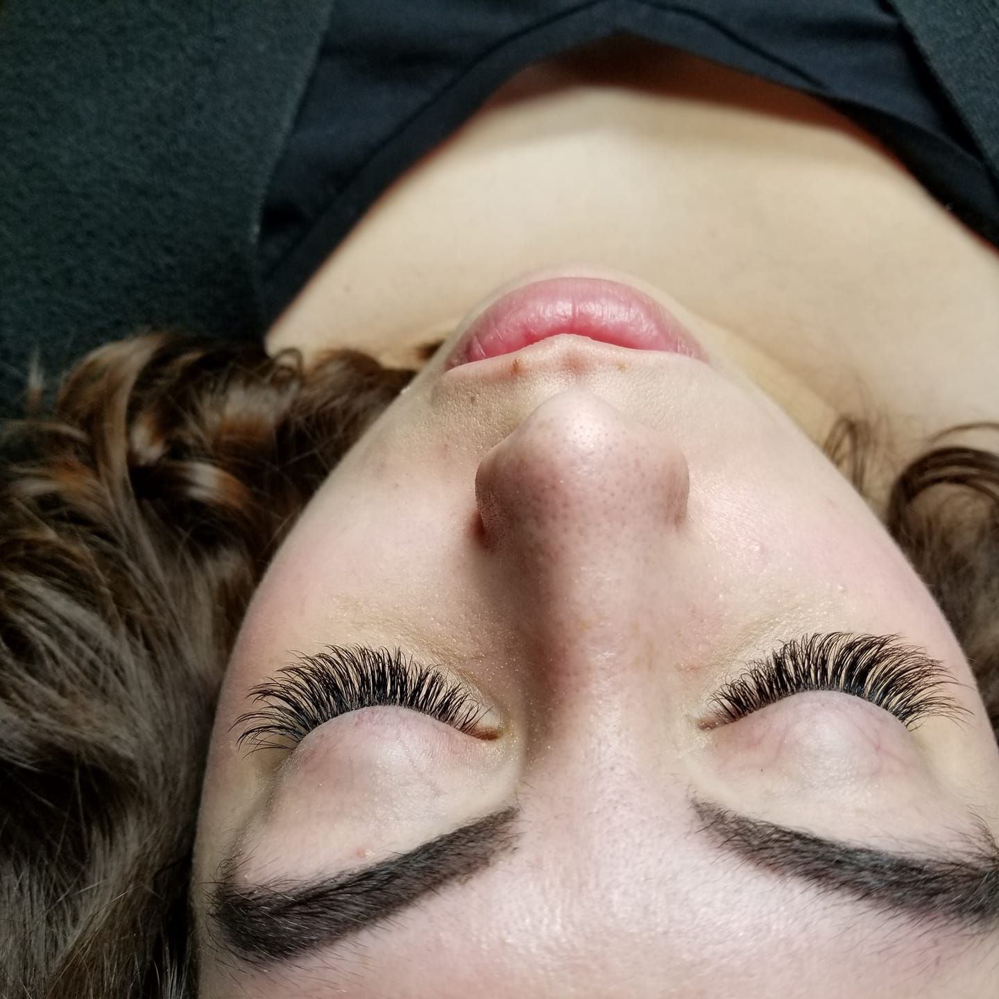 A woman with long eyelashes is laying down with her eyes closed.