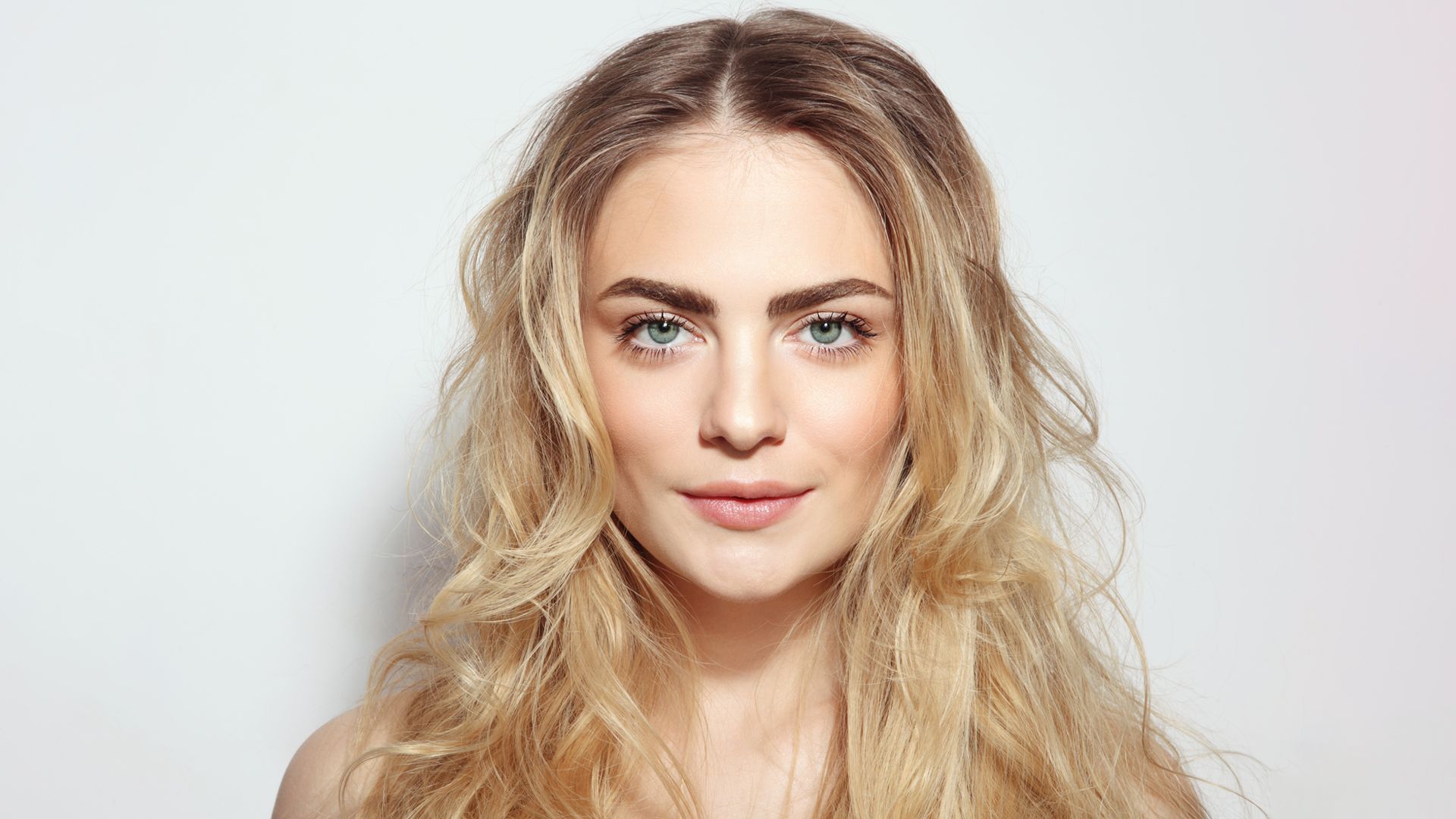 A woman with long blonde hair and blue eyes is looking at the camera.