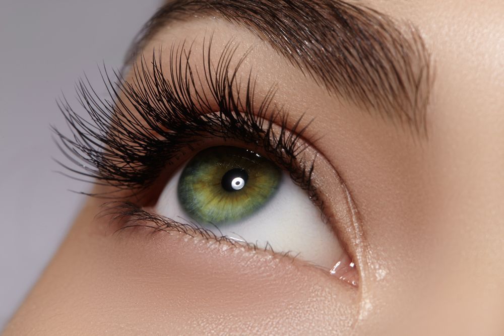 A close up of a woman 's green eye with long eyelashes.