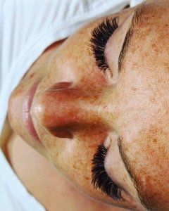 A close up of a woman 's face with long eyelashes and freckles.