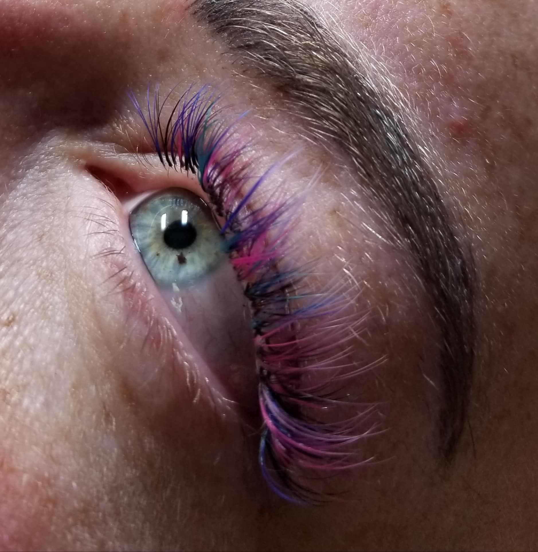 A close up of a woman 's eye with pink and blue eyelashes