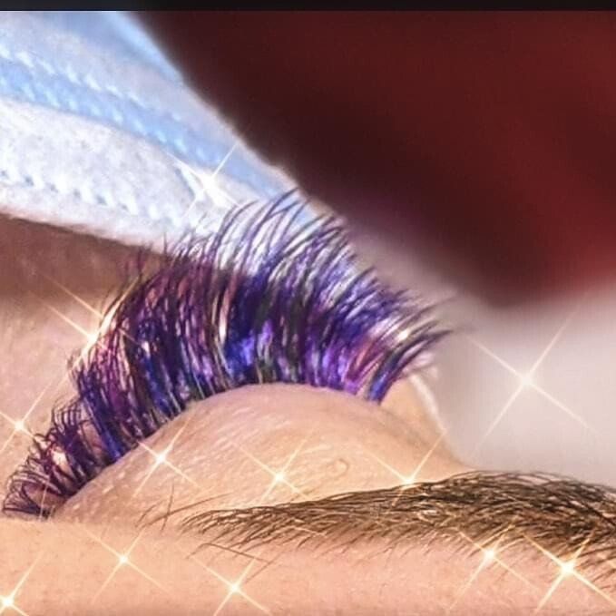 A close up of a woman 's eye with purple eyelashes.