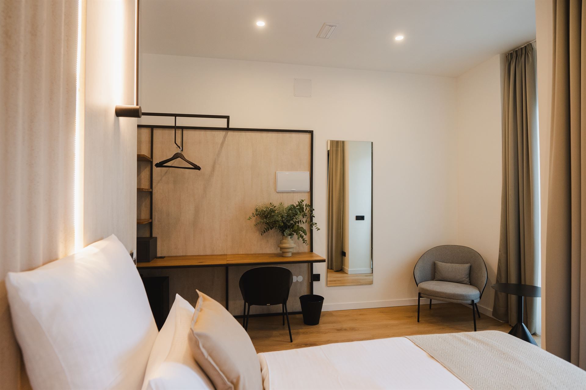 A hotel room with a bed , chair , desk and mirror.