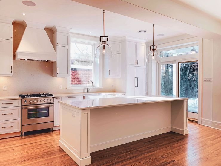 Cuisine blanche lumineuse avec électroménagers en acier inoxydable, grand îlot central, plancher en bois et porte vitrée donnant sur l'extérieur.