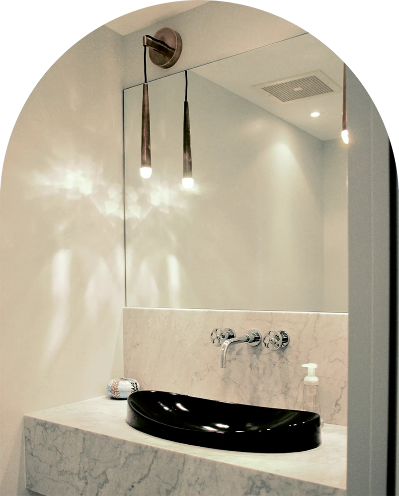 Salle de bains avec lavabo noir, comptoir en marbre, grand miroir et luminaires suspendus.