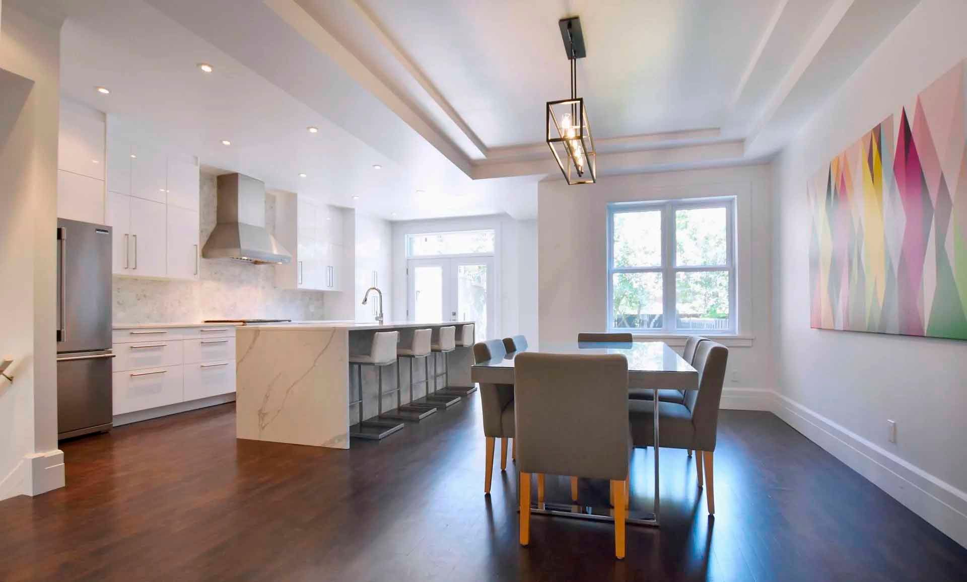 Cuisine et salle à manger modernes avec placards blancs, îlot en marbre, parquet foncé et grande fenêtre.