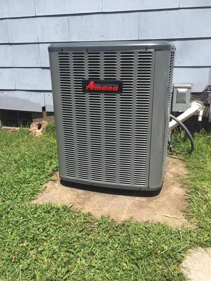 An air conditioner is sitting in the grass in front of a house.