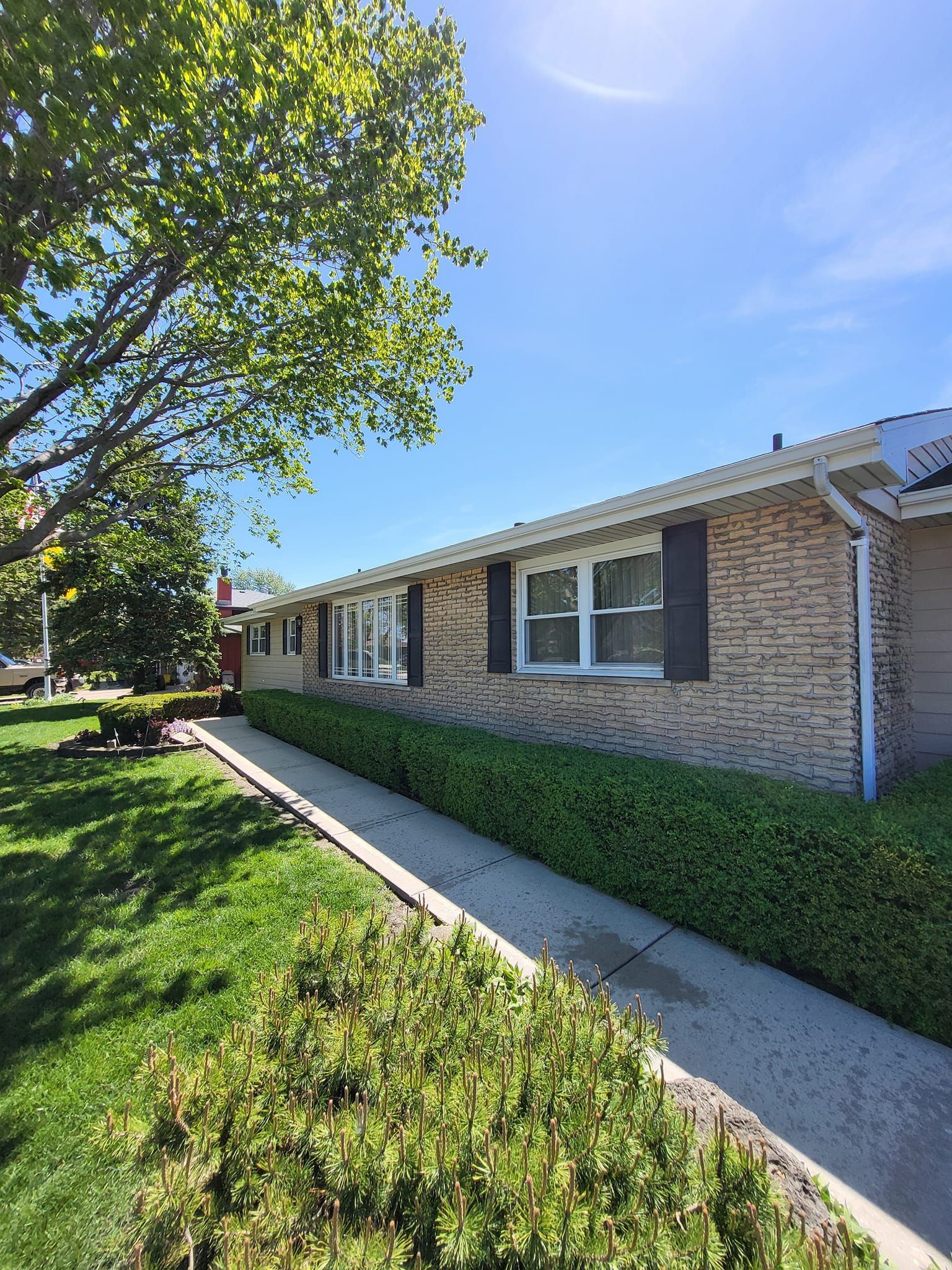 A brick house with black shutters and a sidewalk in front of it.