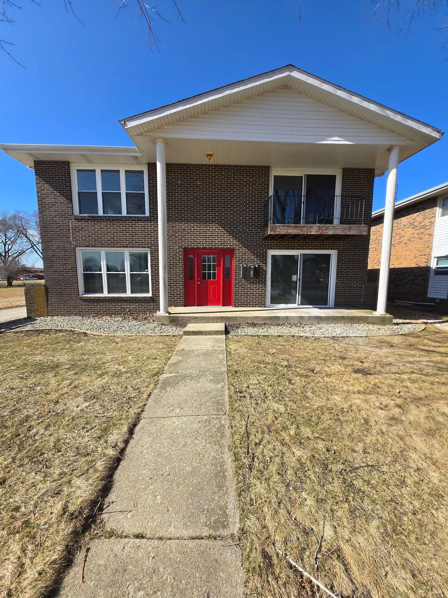 A large brick house with a red door and a walkway leading to it.