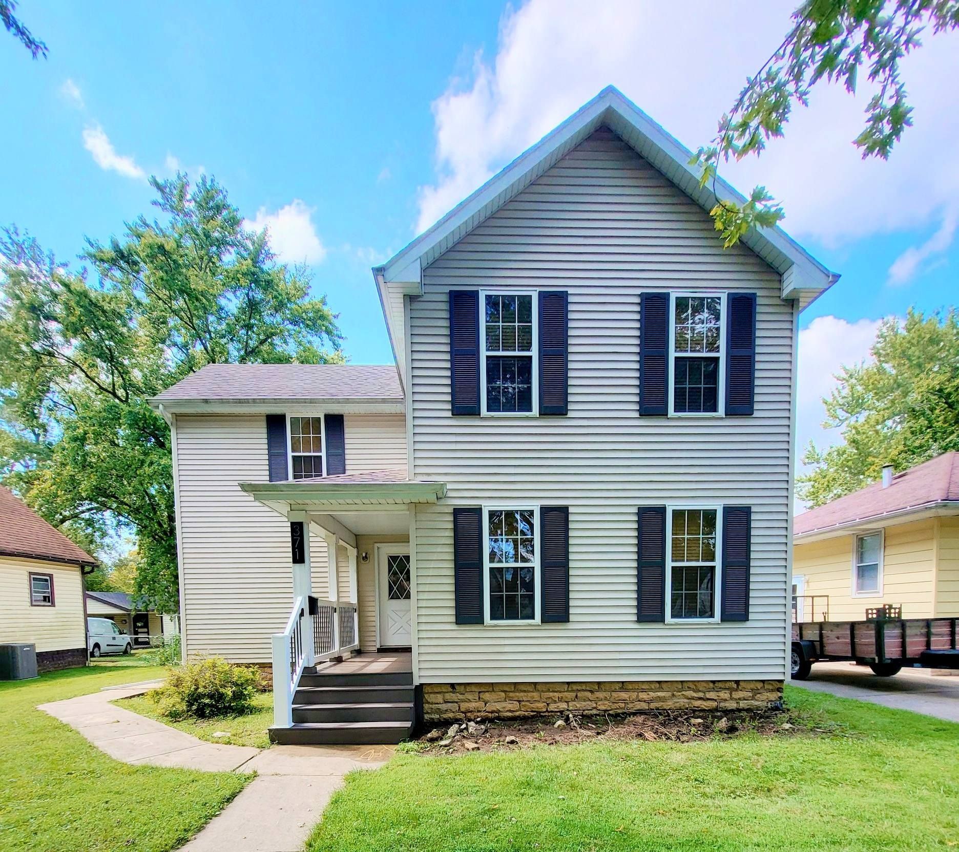 A white house with black shutters is sitting on top of a lush green lawn.