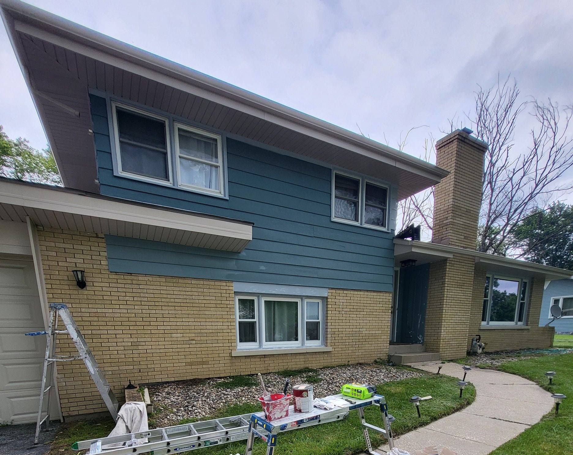 A house is being painted blue with a ladder in front of it.