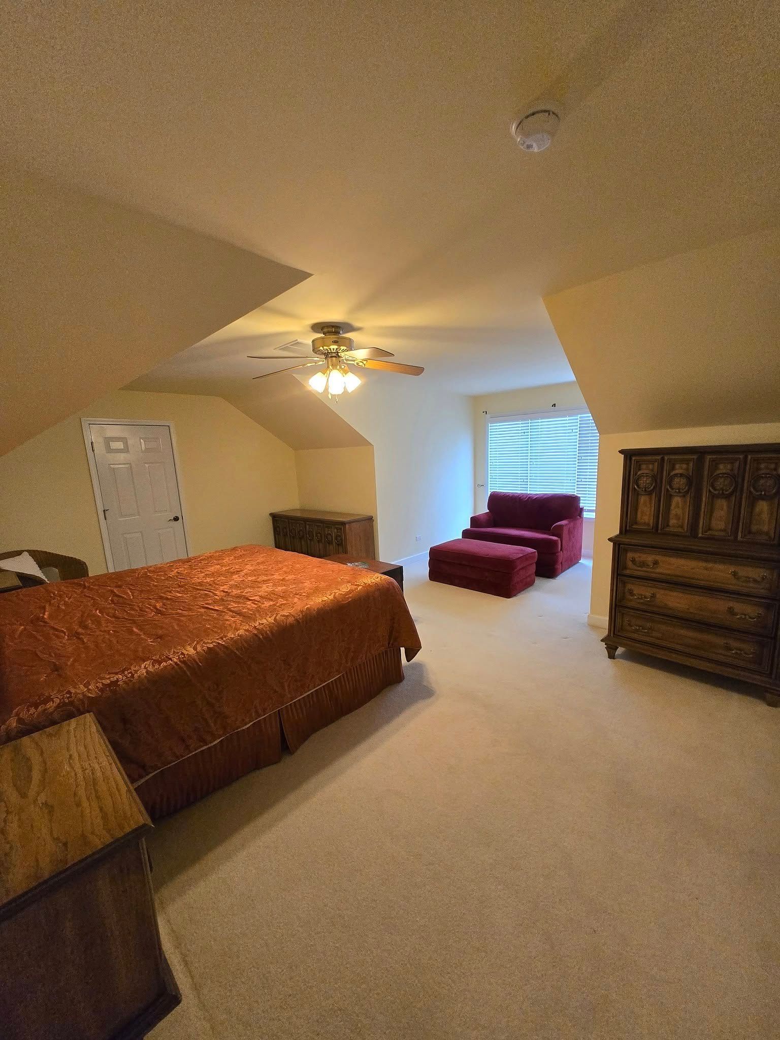 A bedroom with a bed , dresser , chair and ceiling fan.