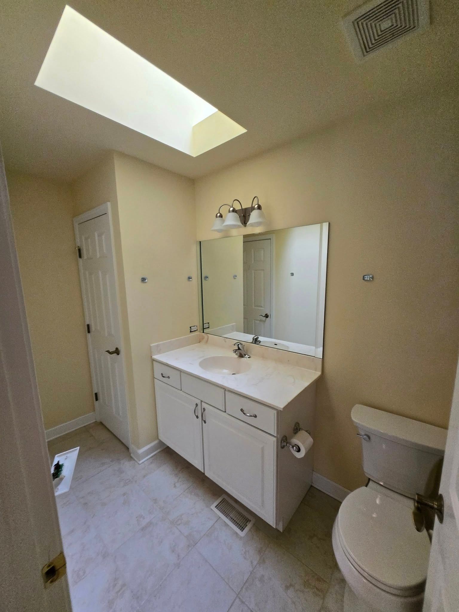 A bathroom with a toilet , sink , mirror and skylight.