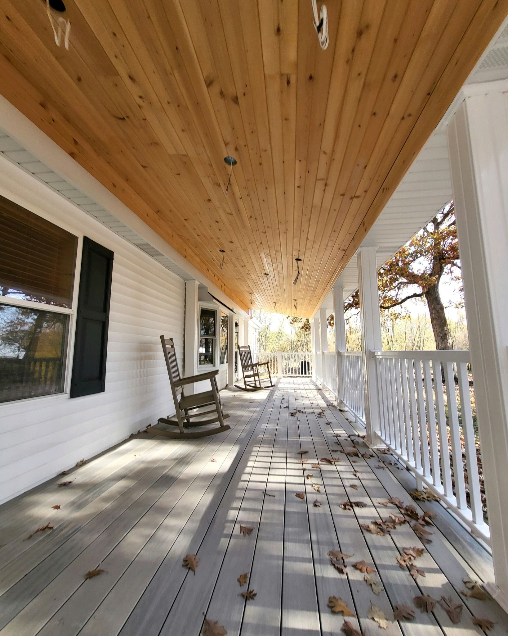 A long porch with a wooden ceiling and rocking chairs