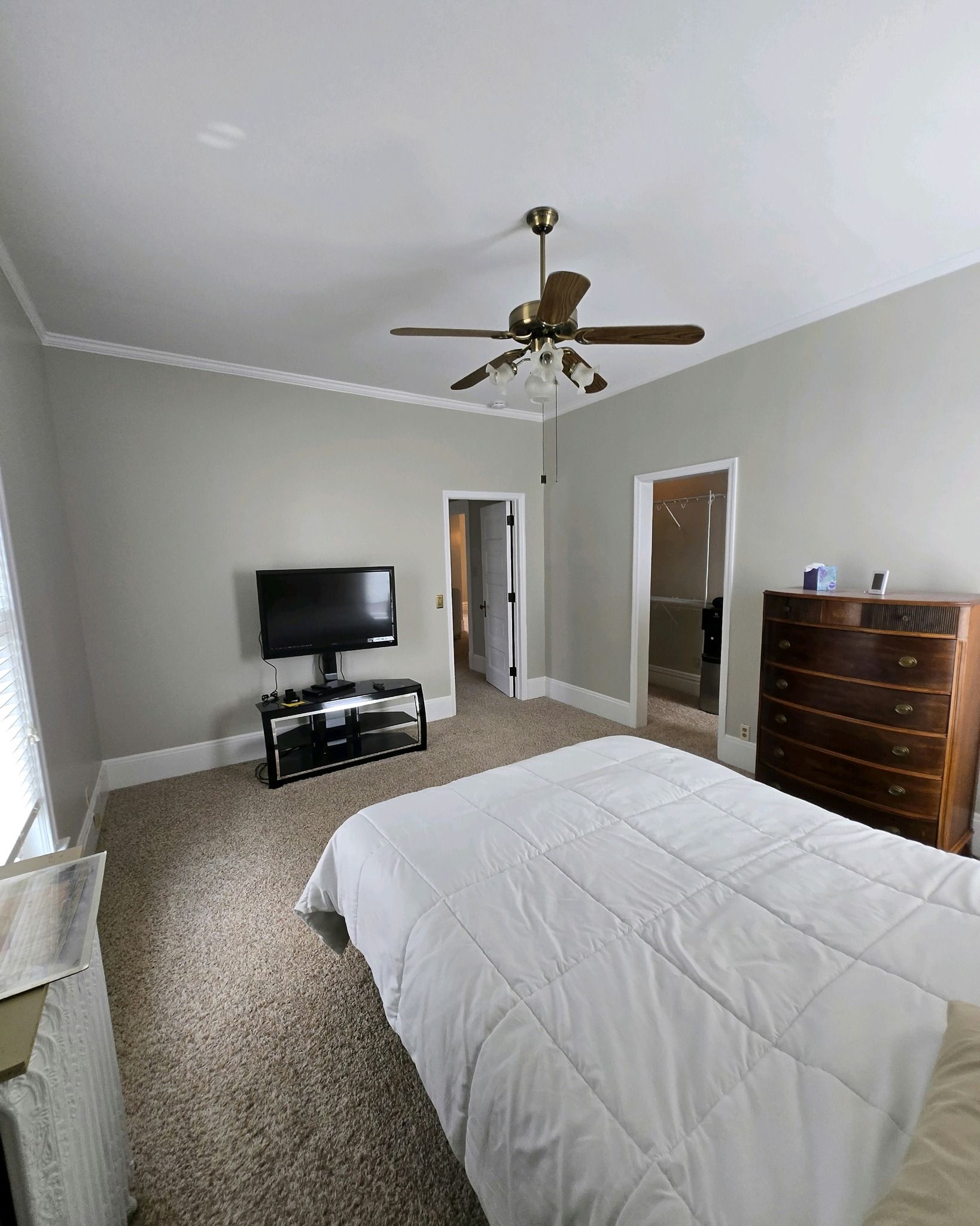 A bedroom with a bed , dresser , television and ceiling fan.