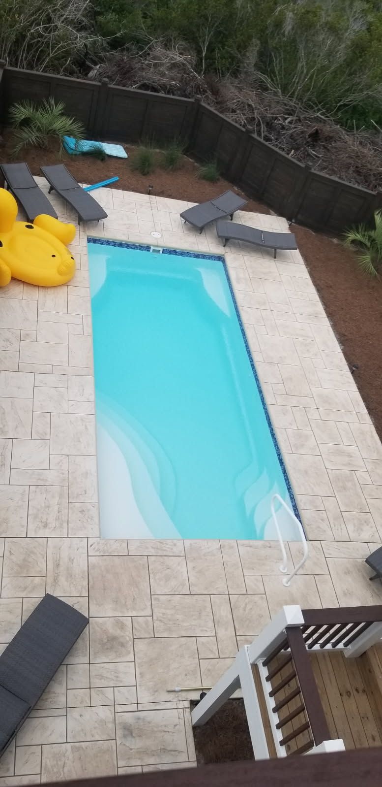 An aerial view of a swimming pool surrounded by chairs and a yellow duck float.