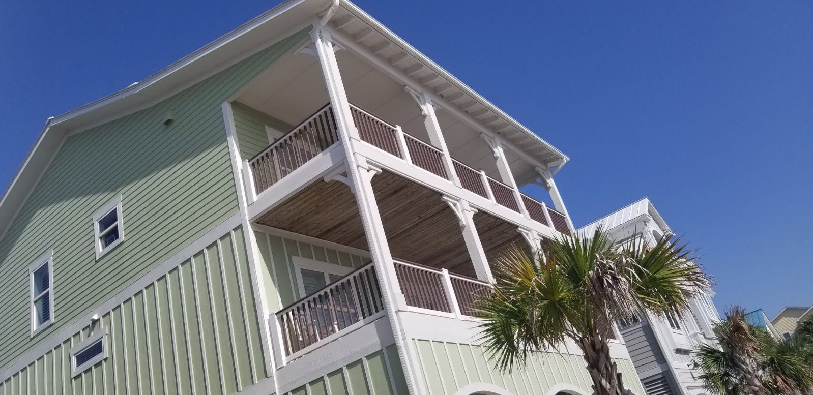 A large green house with a lot of balconies and a palm tree in front of it.