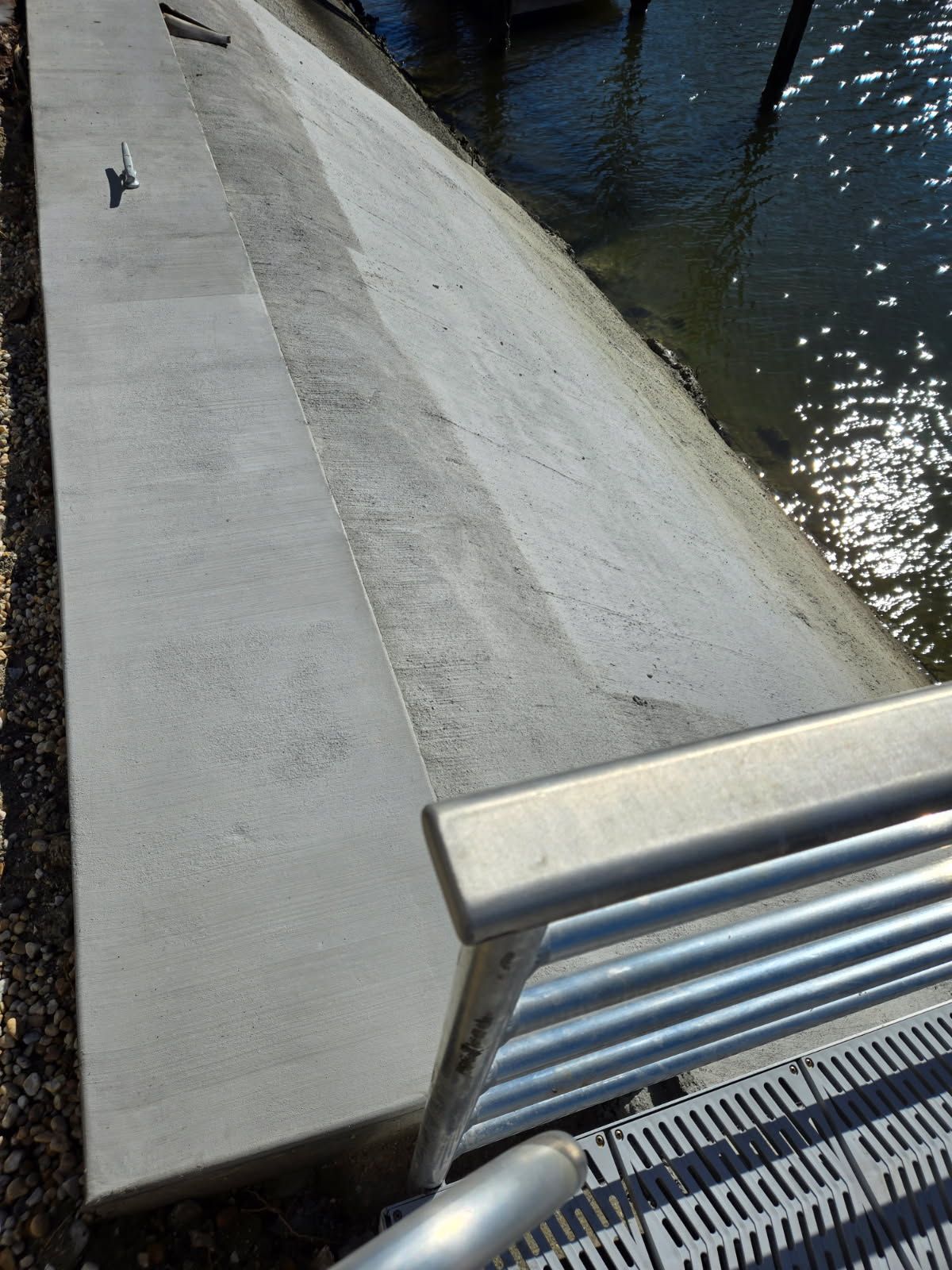A concrete walkway next to a body of water with a metal railing.