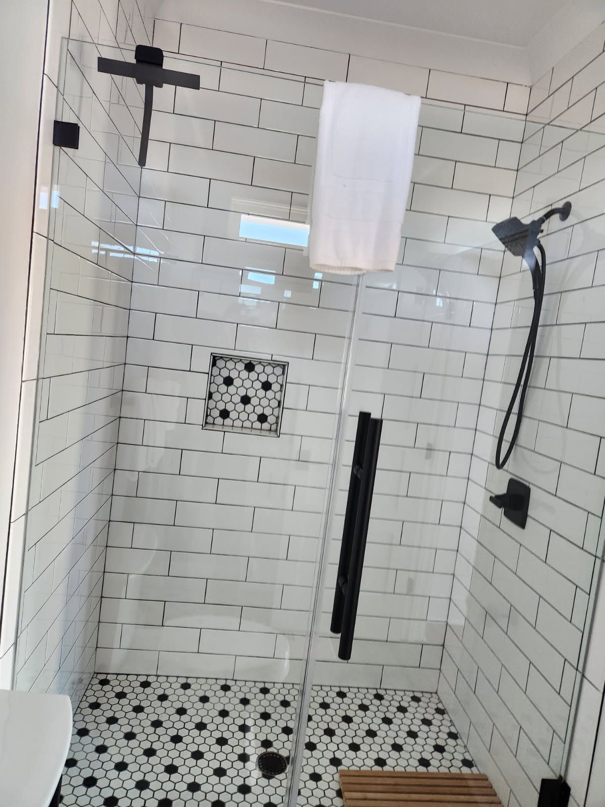 A bathroom with white brick walls and black and white tiles has a walk in shower with a glass door.