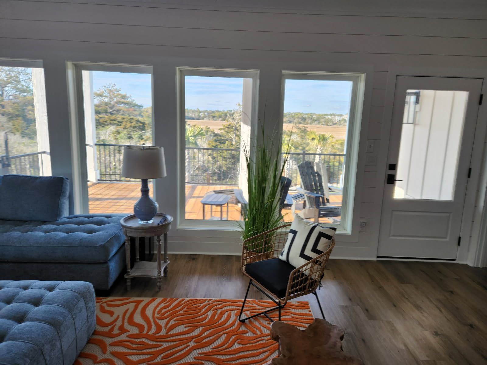A living room with a couch , chair , ottoman , lamp and many windows.
